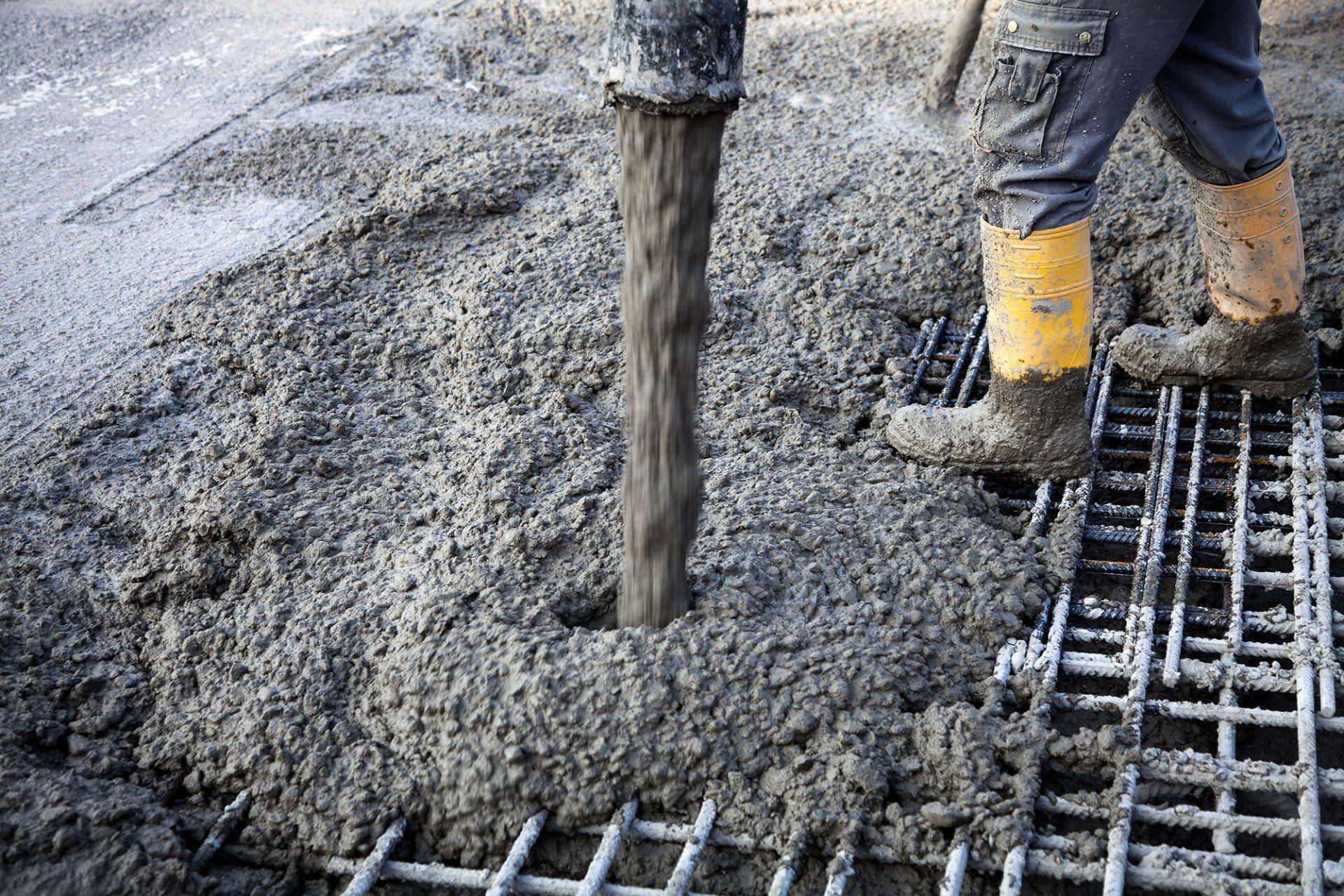 Concrete being poured onto steel rebar by a worker in yellow boots at a construction site