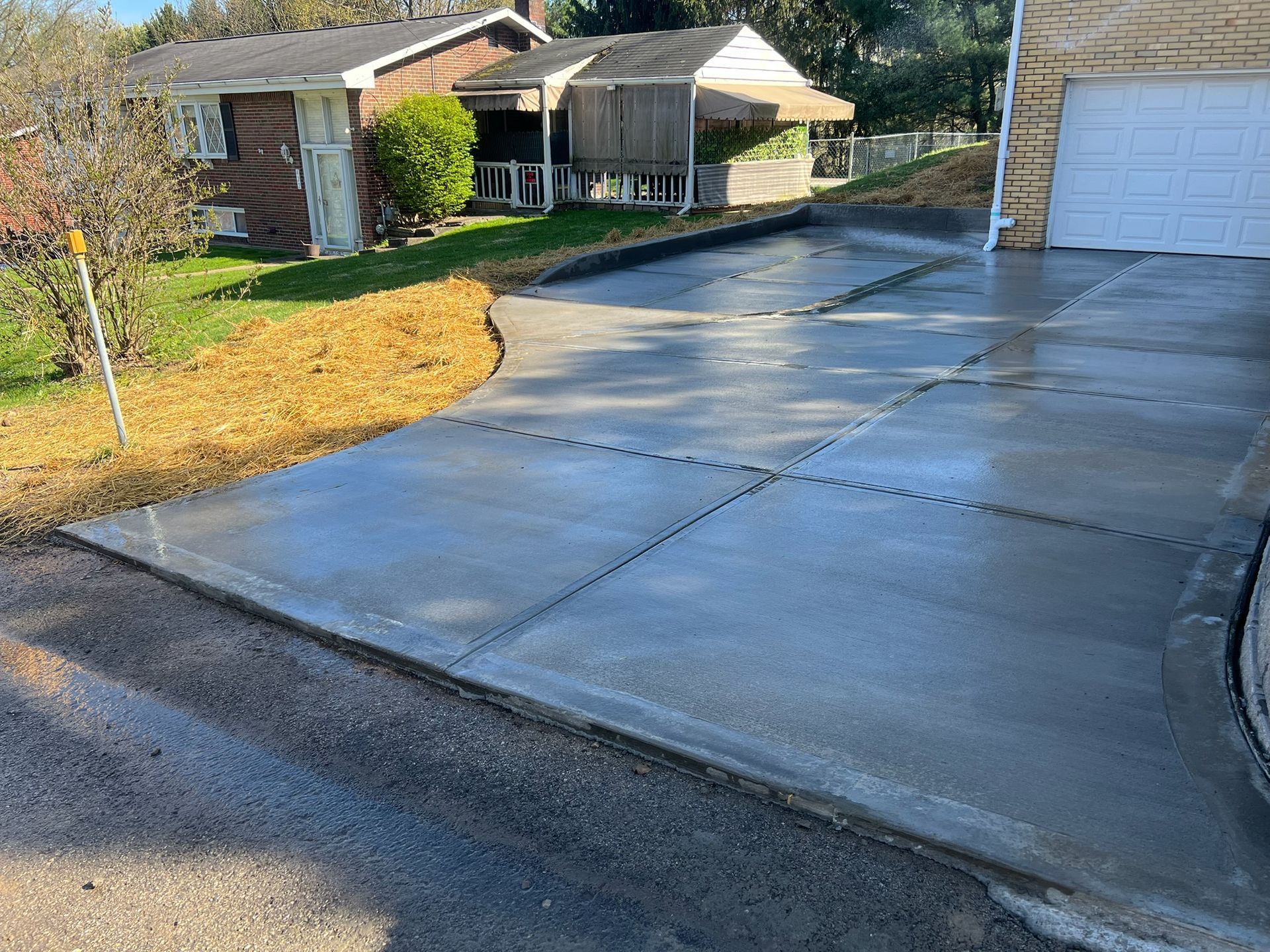 Concrete driveway leading to a house and garage, with green lawn and trees on a sunny day