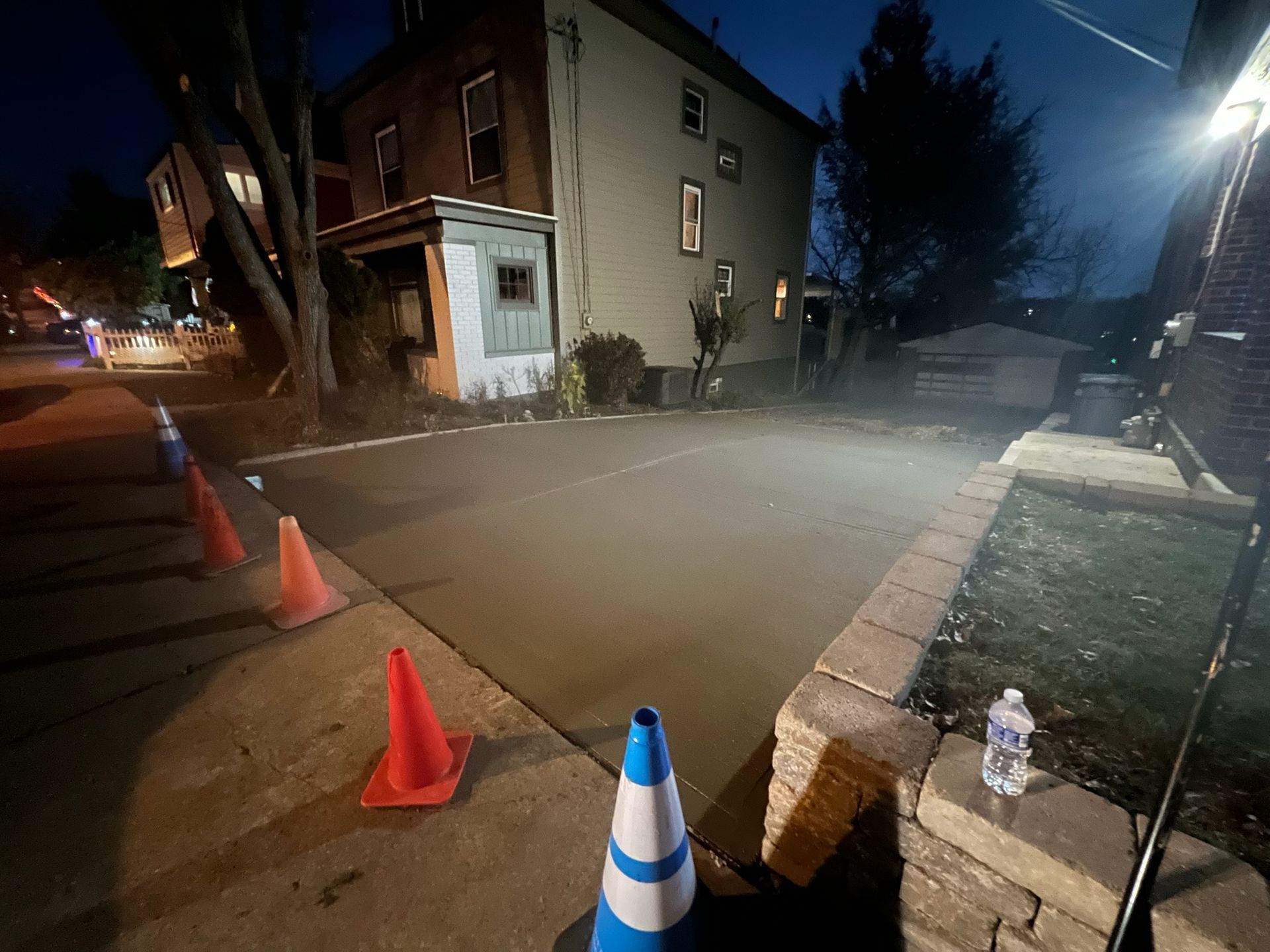 Night street scene with orange cones, a blue-white cone, and a house beside a misty road