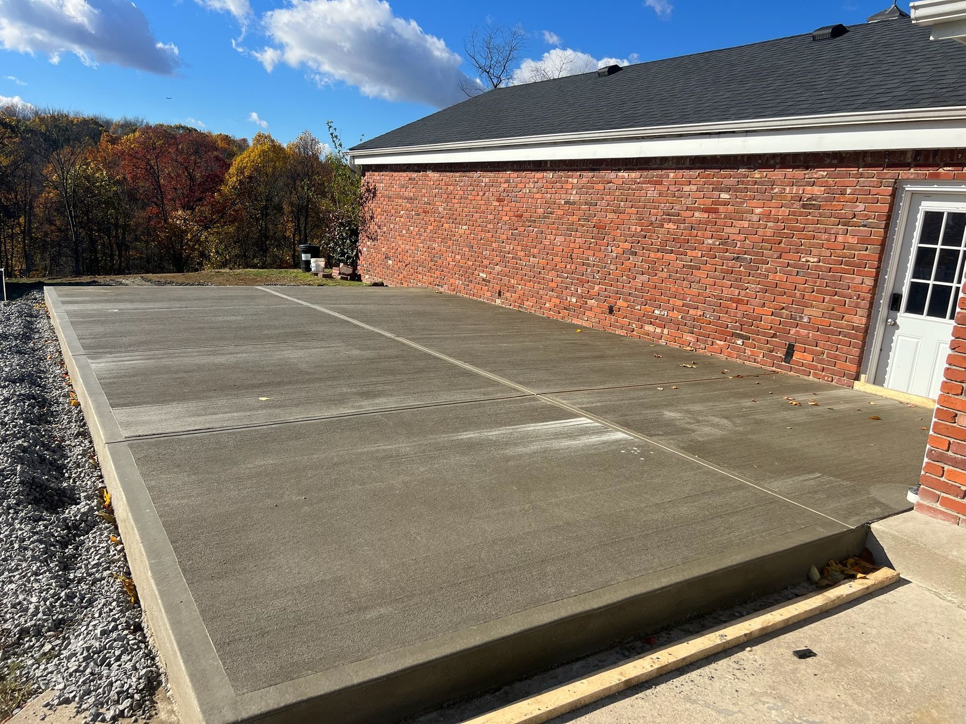 Concrete patio beside a red brick house under a blue sky, with gravel edging and a white side door.