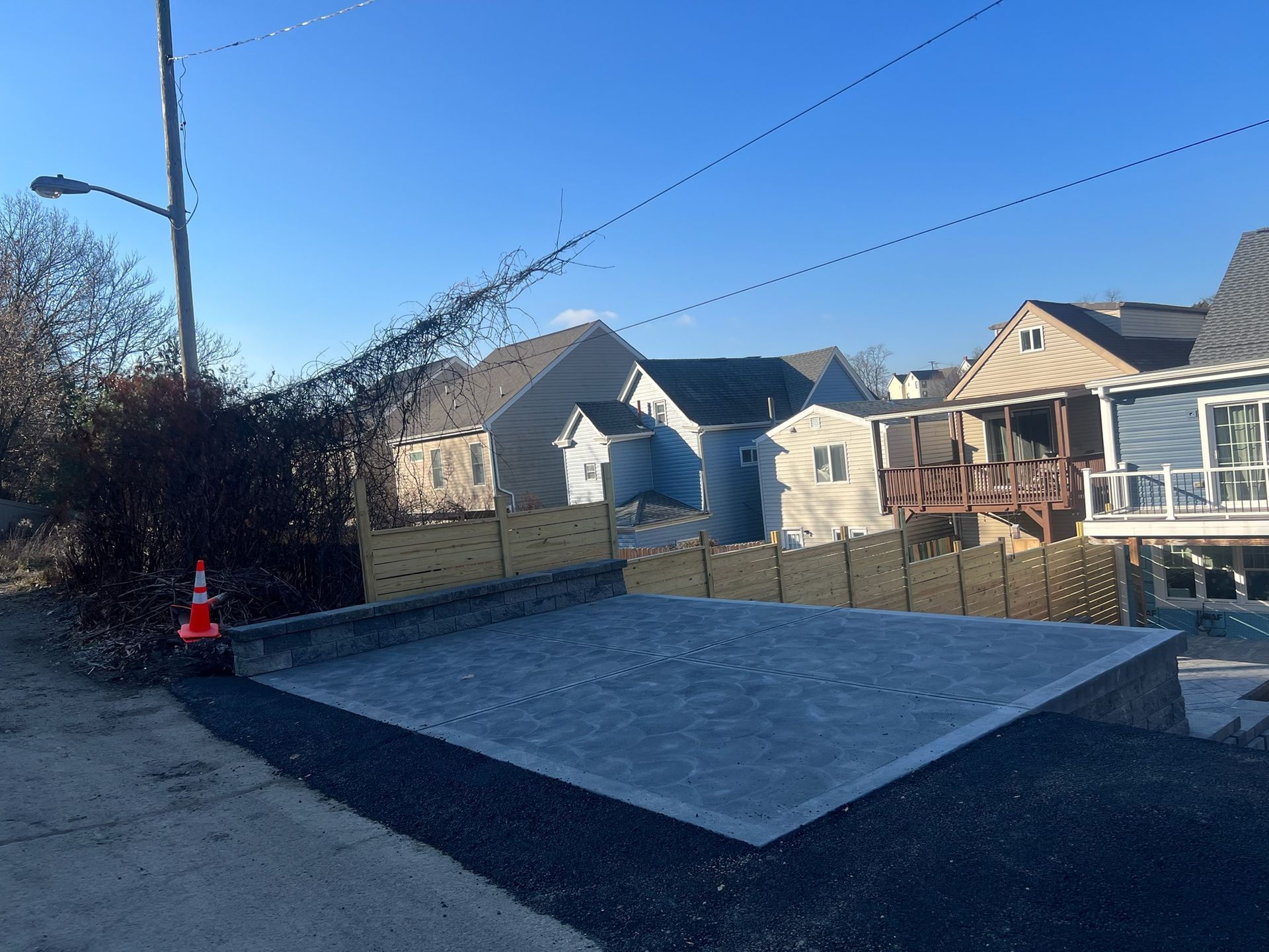 Driveway under construction beside suburban houses, with fresh gray concrete and an orange cone.