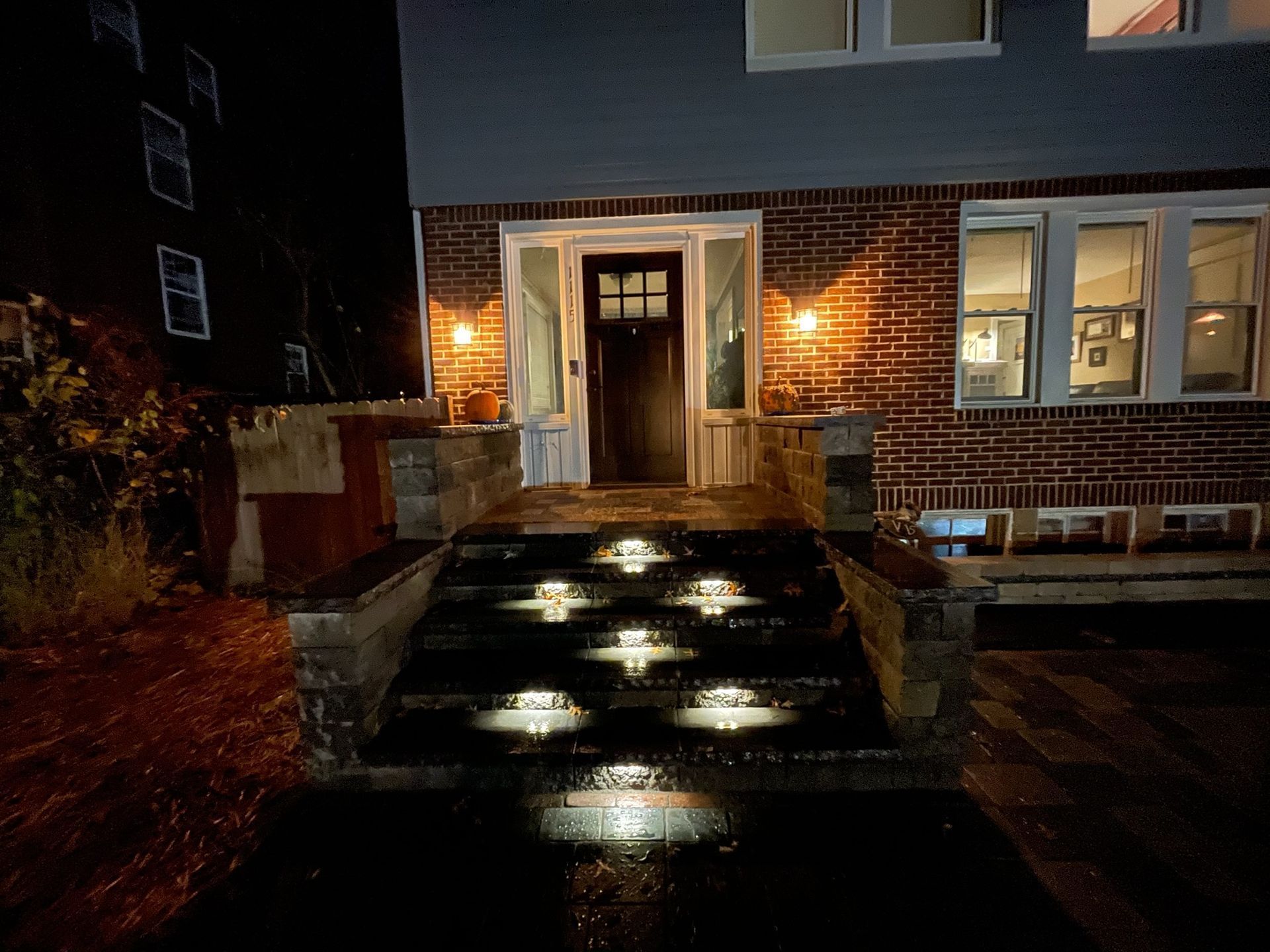 Front entrance of a brick building at night, with lit path lights and warm porch lamps.