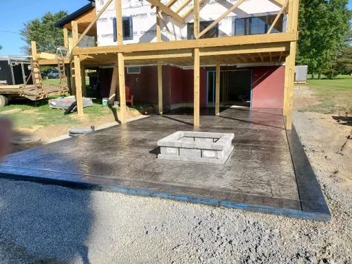 House under construction with a raised wooden deck, concrete patio, and gravel foreground
