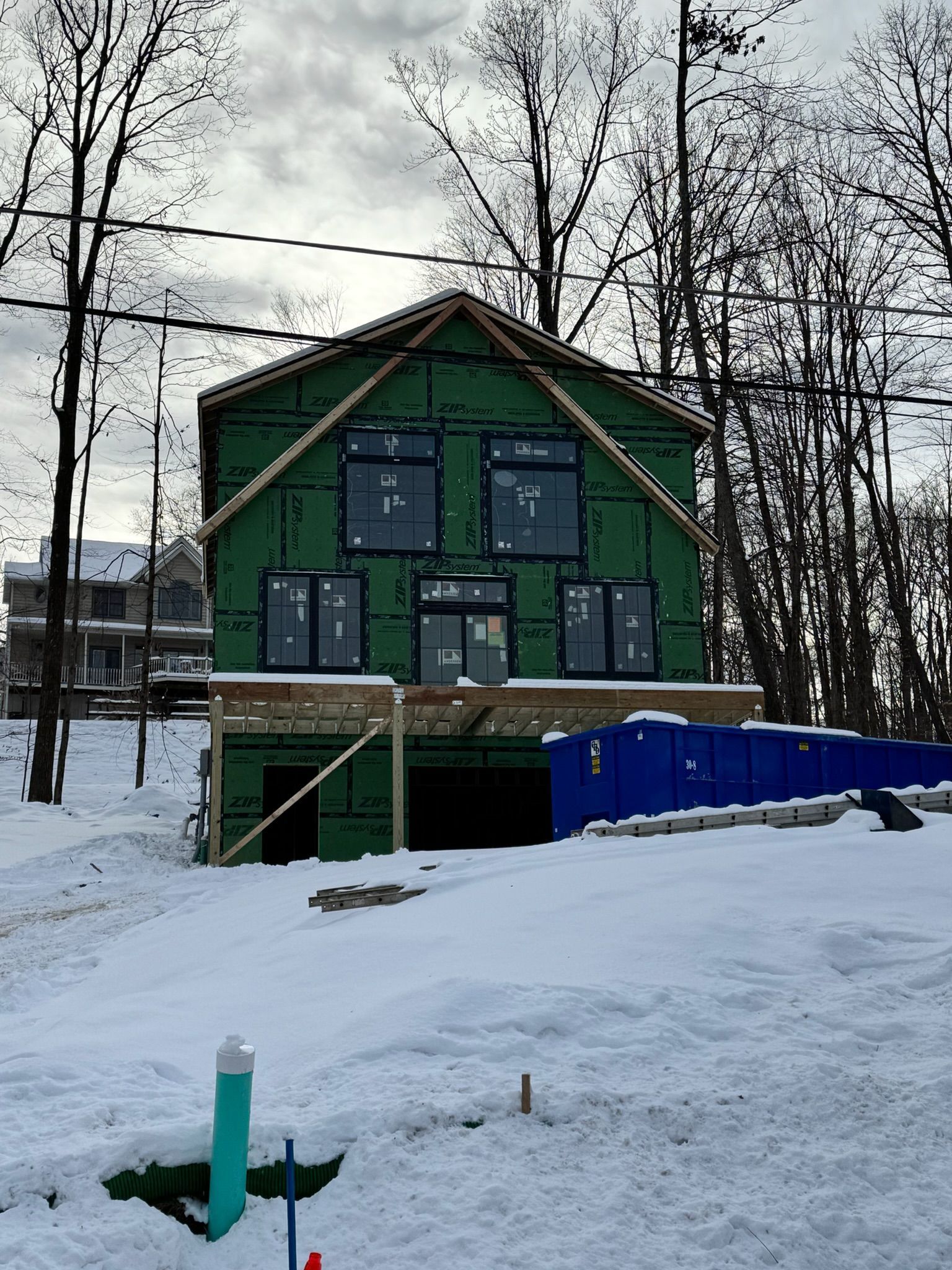 Green house under construction in snowy yard, with blue barrier and bare trees in the background.