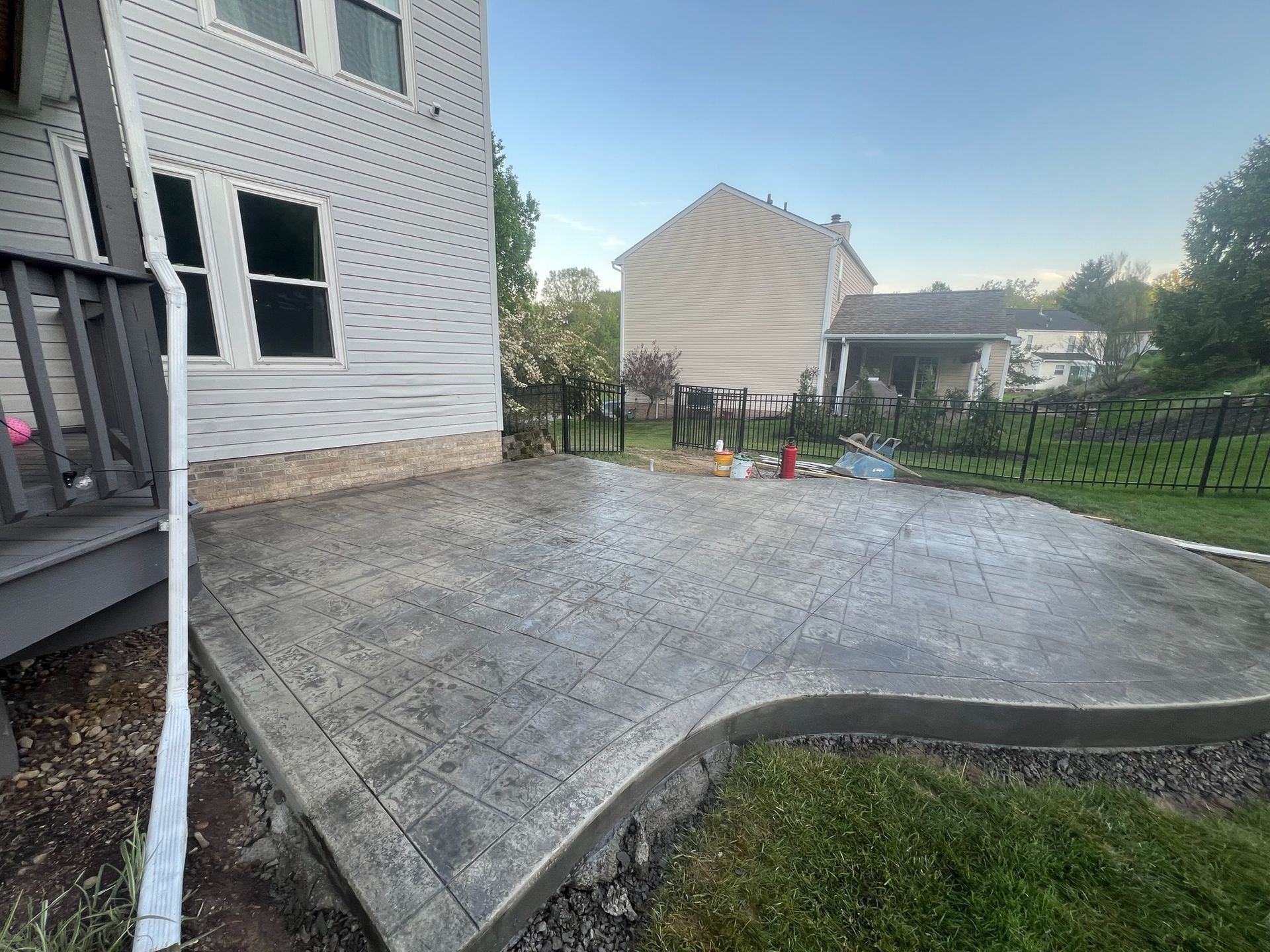 New concrete patio beside a white house, with a curved edge and fenced backyard.