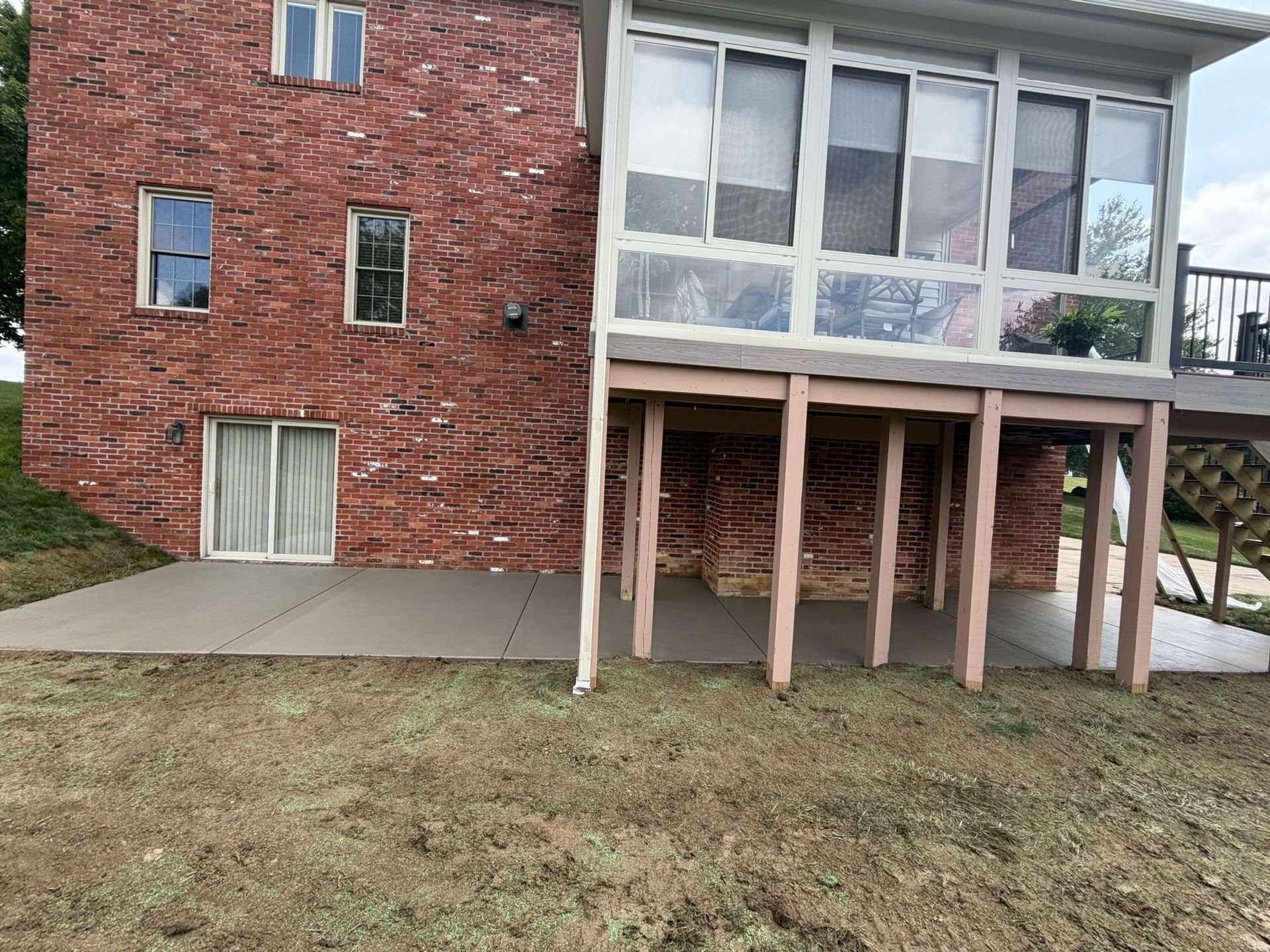 Red brick house with glass-enclosed upper level and raised deck on wooden posts above a grassy yard