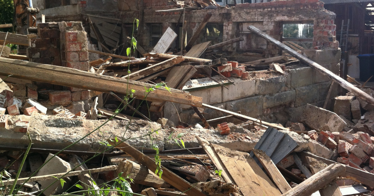 Collapsed building rubble with broken wooden beams, bricks, and debris scattered across the site