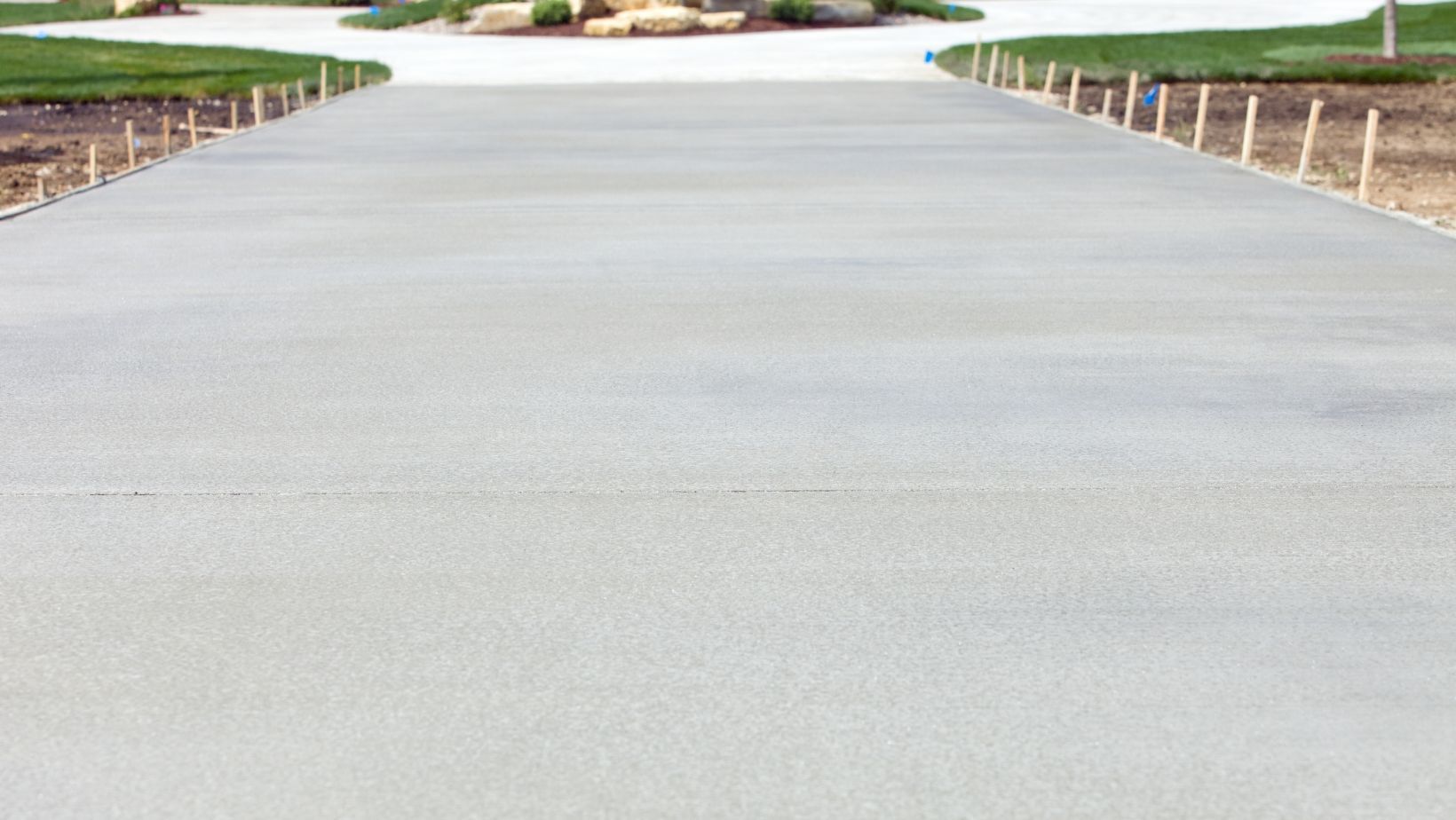 Newly poured concrete road leading toward a grassy area and curb lines