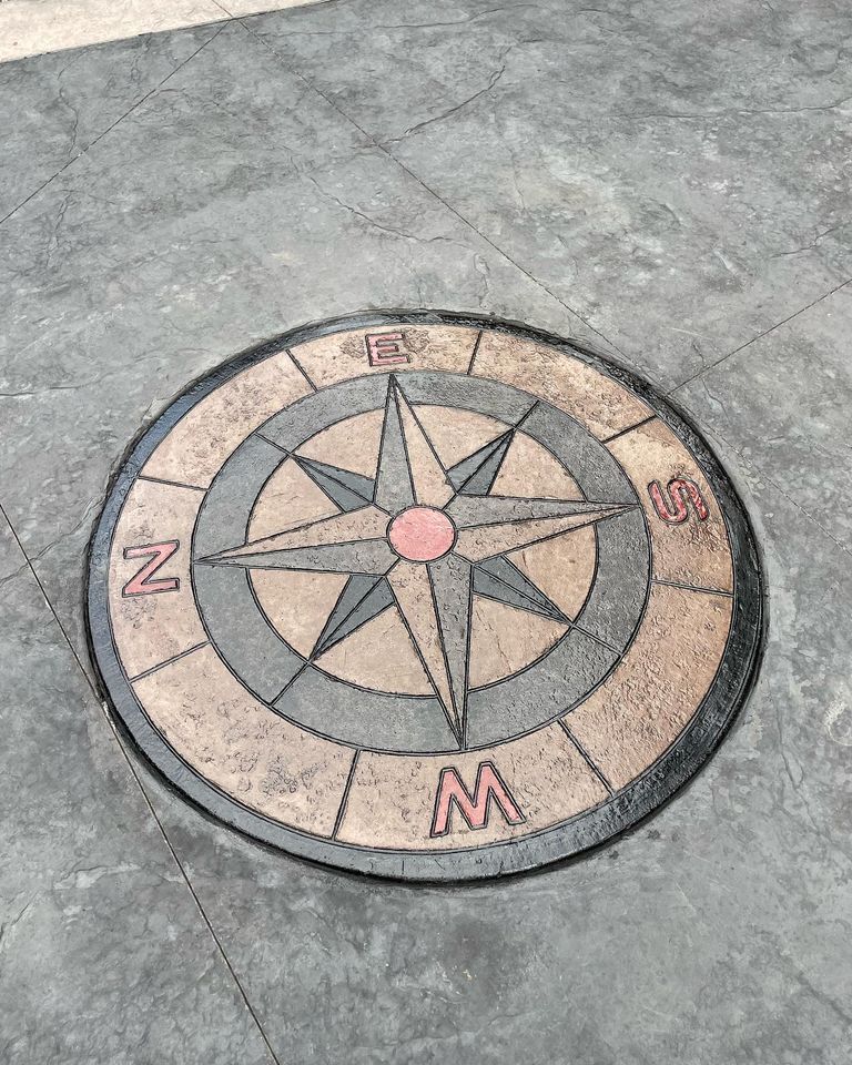 Compass rose mosaic on gray pavement, marked with N, E, S, and W.
