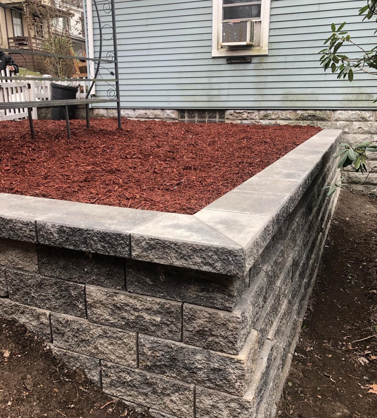 Raised stone planter with red mulch beside a house wall