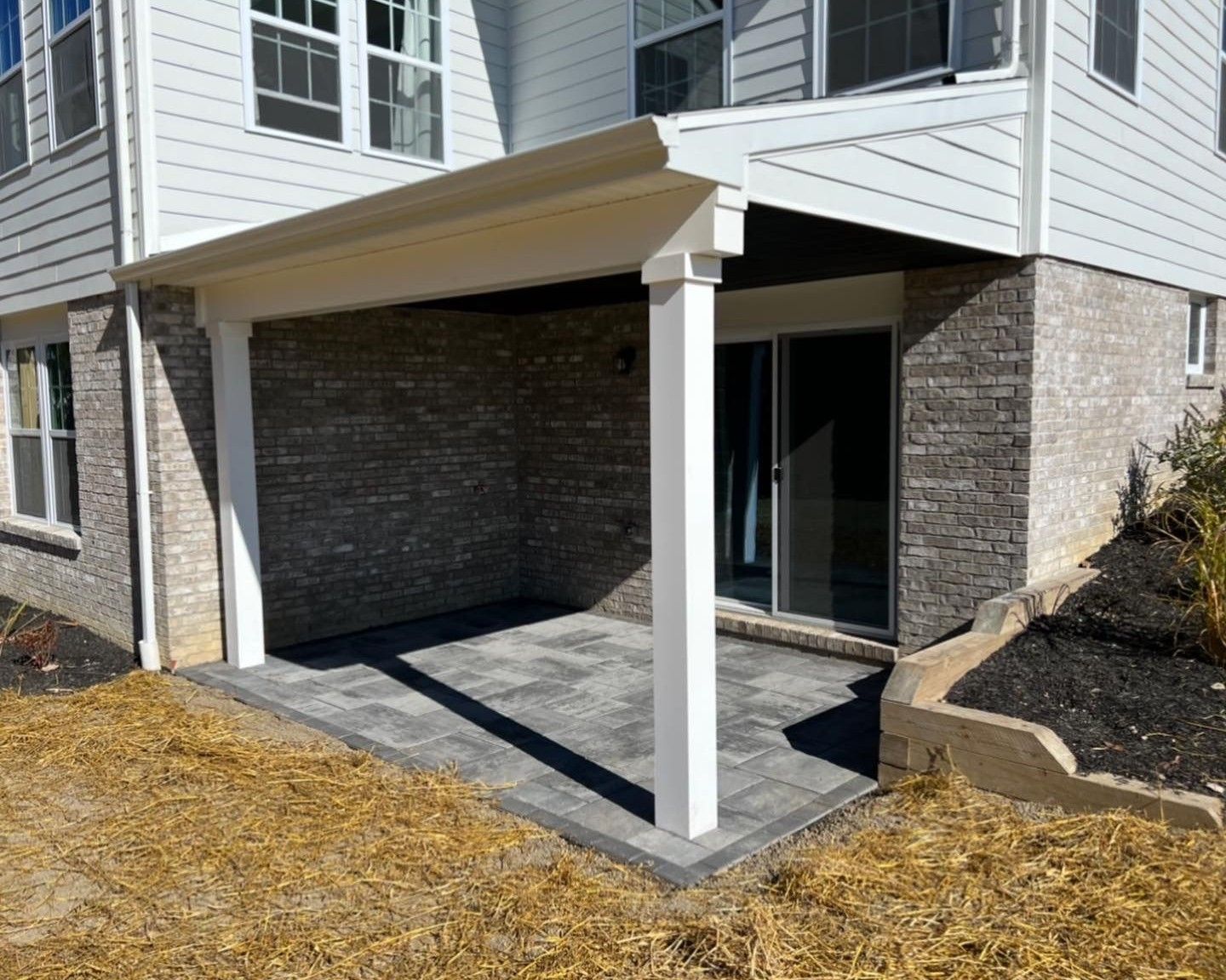 Covered apartment patio with tan awning, white columns, brick walls, and a sliding glass door