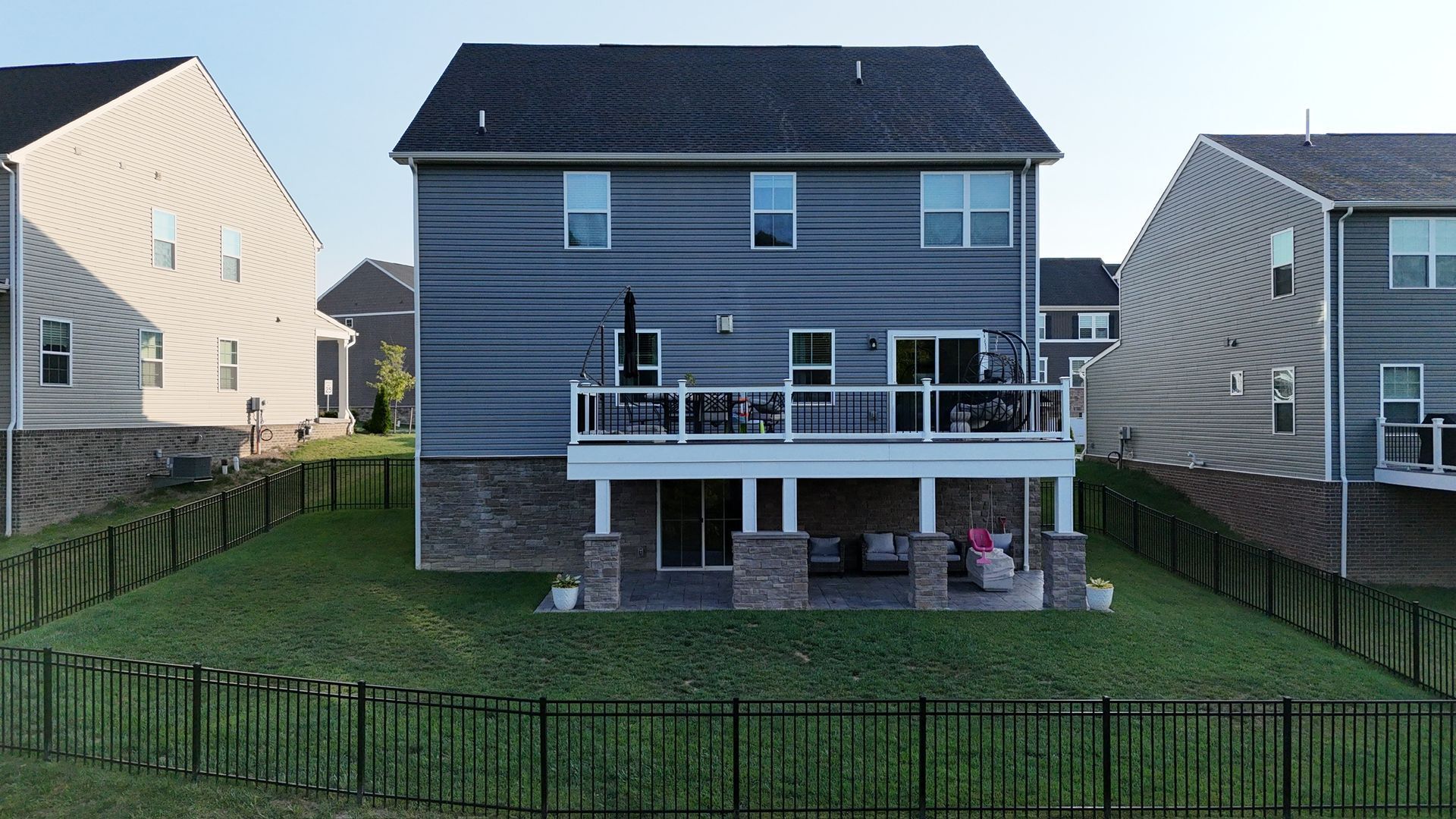 Backyard view of a gray two-story house with a raised deck and fenced lawn