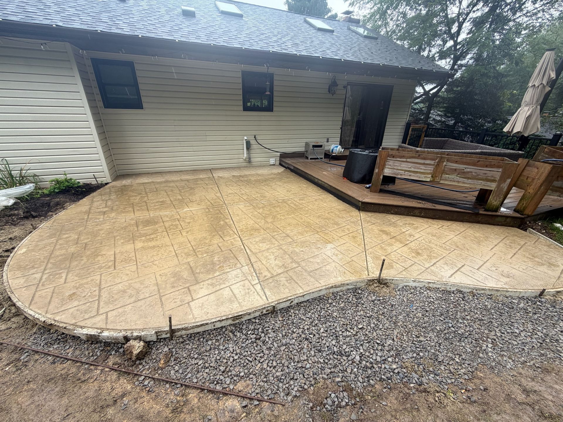 Concrete patio beside a white house, with a black grill and gravel edging in the yard.