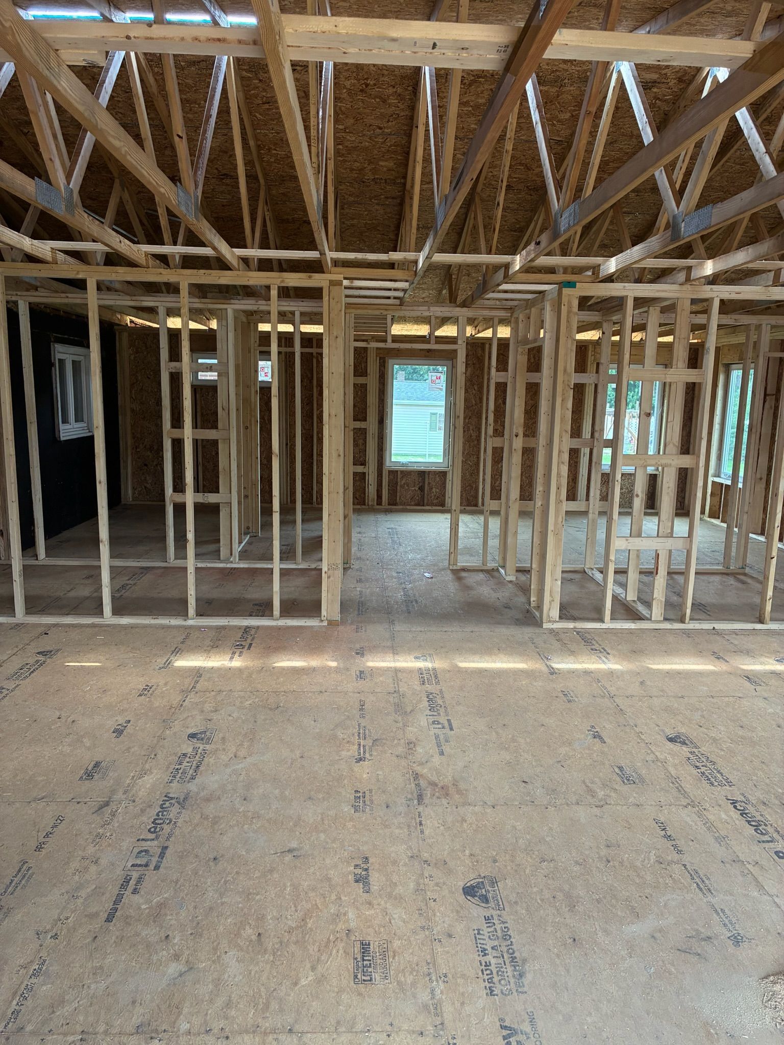 Unfinished house interior with exposed wood framing, open doorways, and plywood subfloor.
