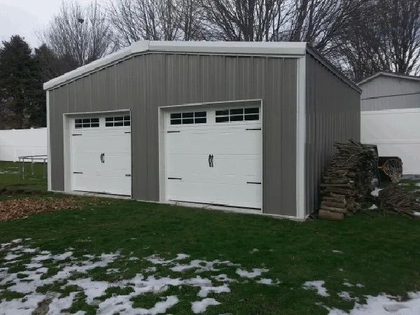 Gray two-car garage with white doors on a snowy lawn