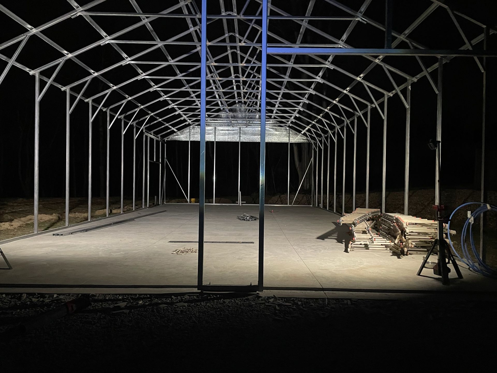 Empty metal-framed pavilion at night with a lit concrete floor and a bicycle on the right.