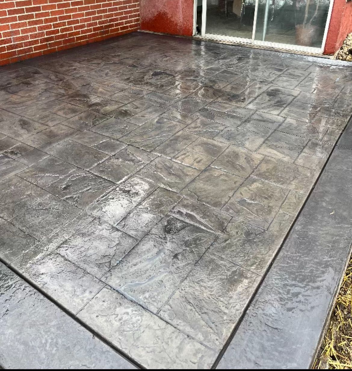 Wet gray tiled patio beside a red brick wall and sliding glass door, with dark border stones.