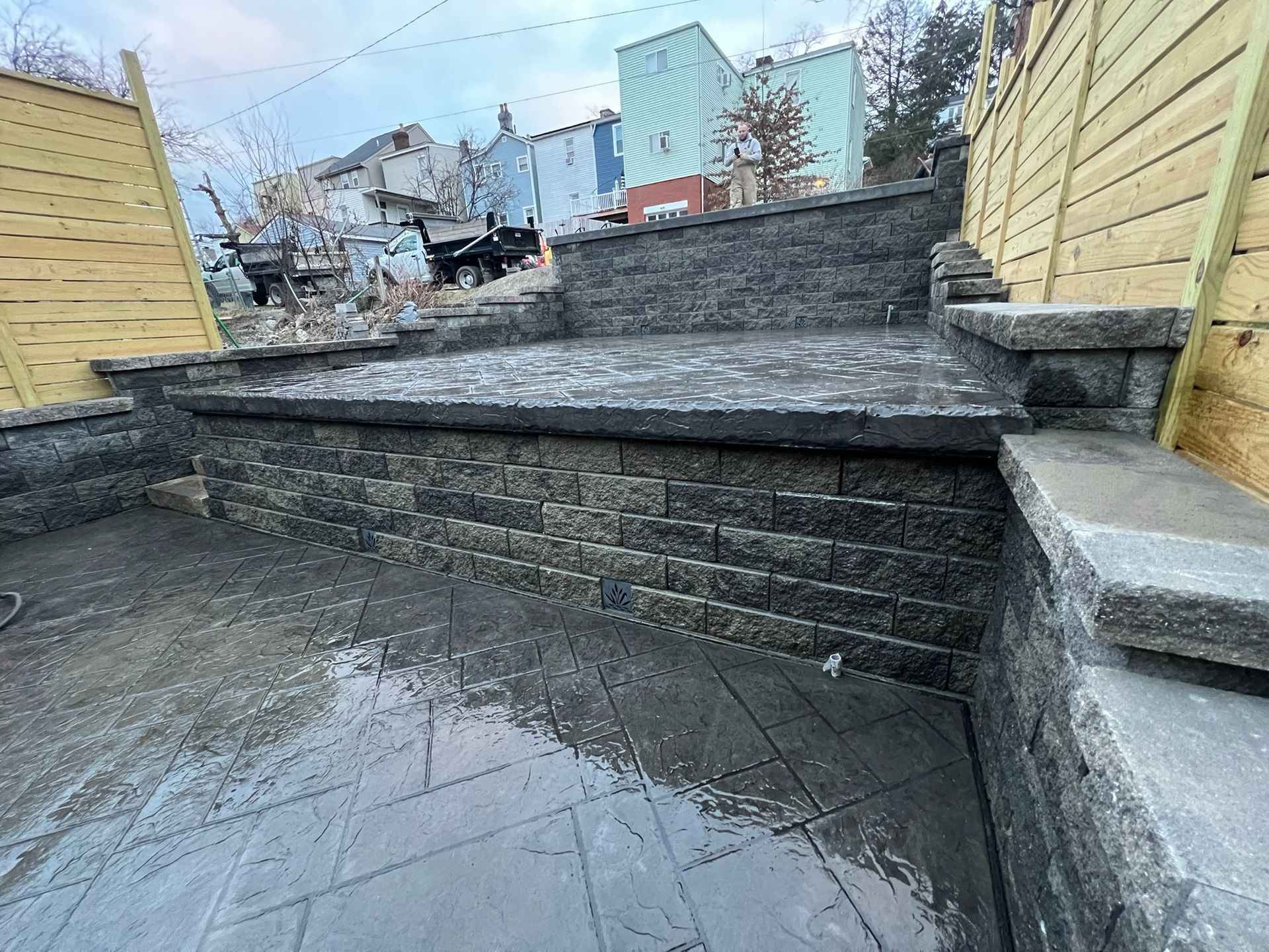 Stone steps and retaining wall in a wet outdoor courtyard with wooden fences and houses in the background