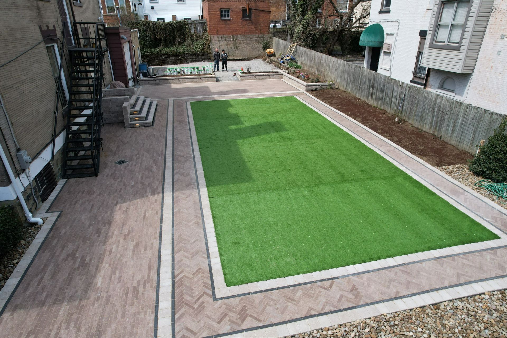 Courtyard with a rectangular artificial grass area bordered by brick walkways and stairs