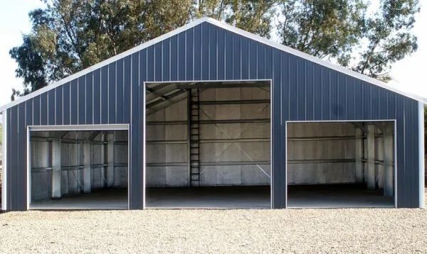 Gray metal barn-style shed with three open bays and a central loft opening on a gravel lot
