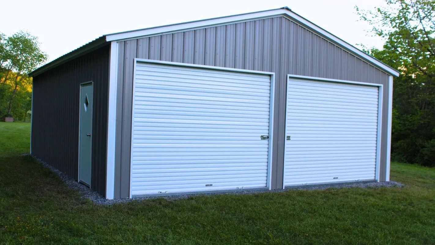 Gray metal storage shed with two white roll-up doors on a grassy lawn