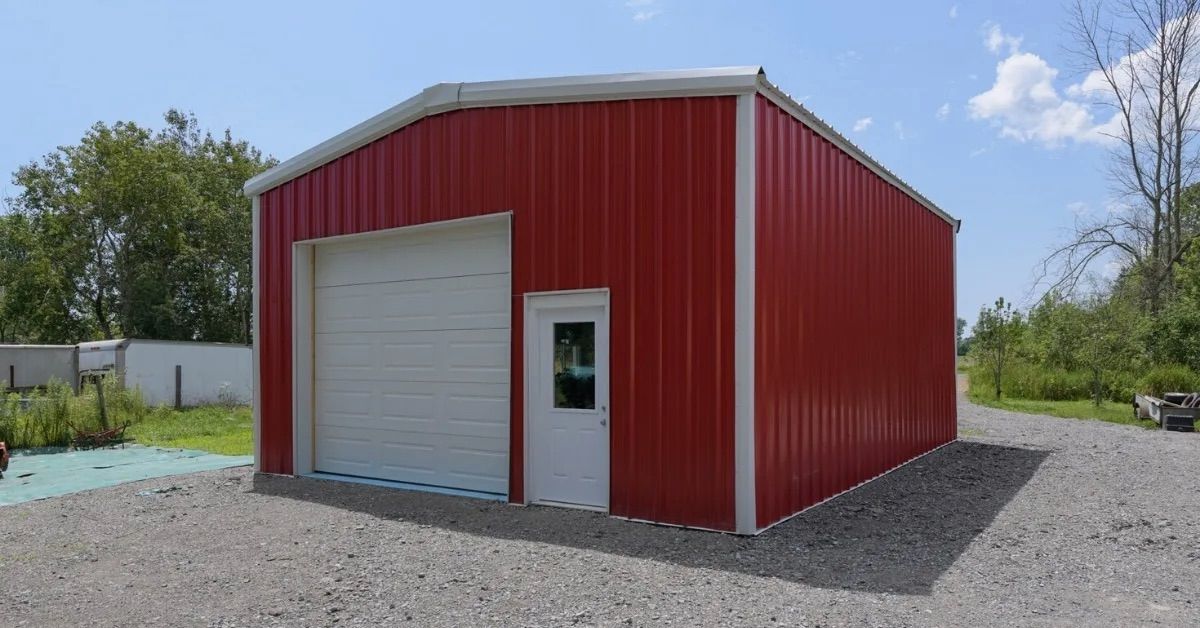 Red metal storage building with white roll-up garage door on a gravel lot under a blue sky