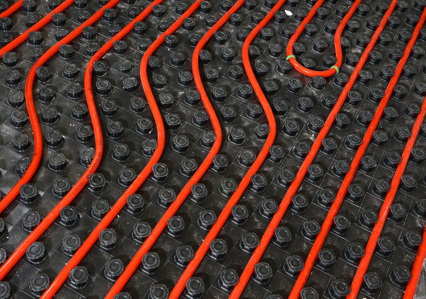 Red radiant floor heating tubes laid in loops over a black dimpled membrane