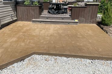Tan paved patio with raised wooden deck and garden borders at the back