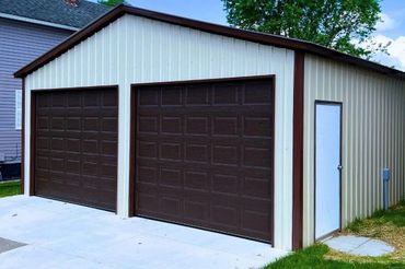 Detached two-car garage with beige siding, brown double doors, and a side entry door on a concrete driveway.