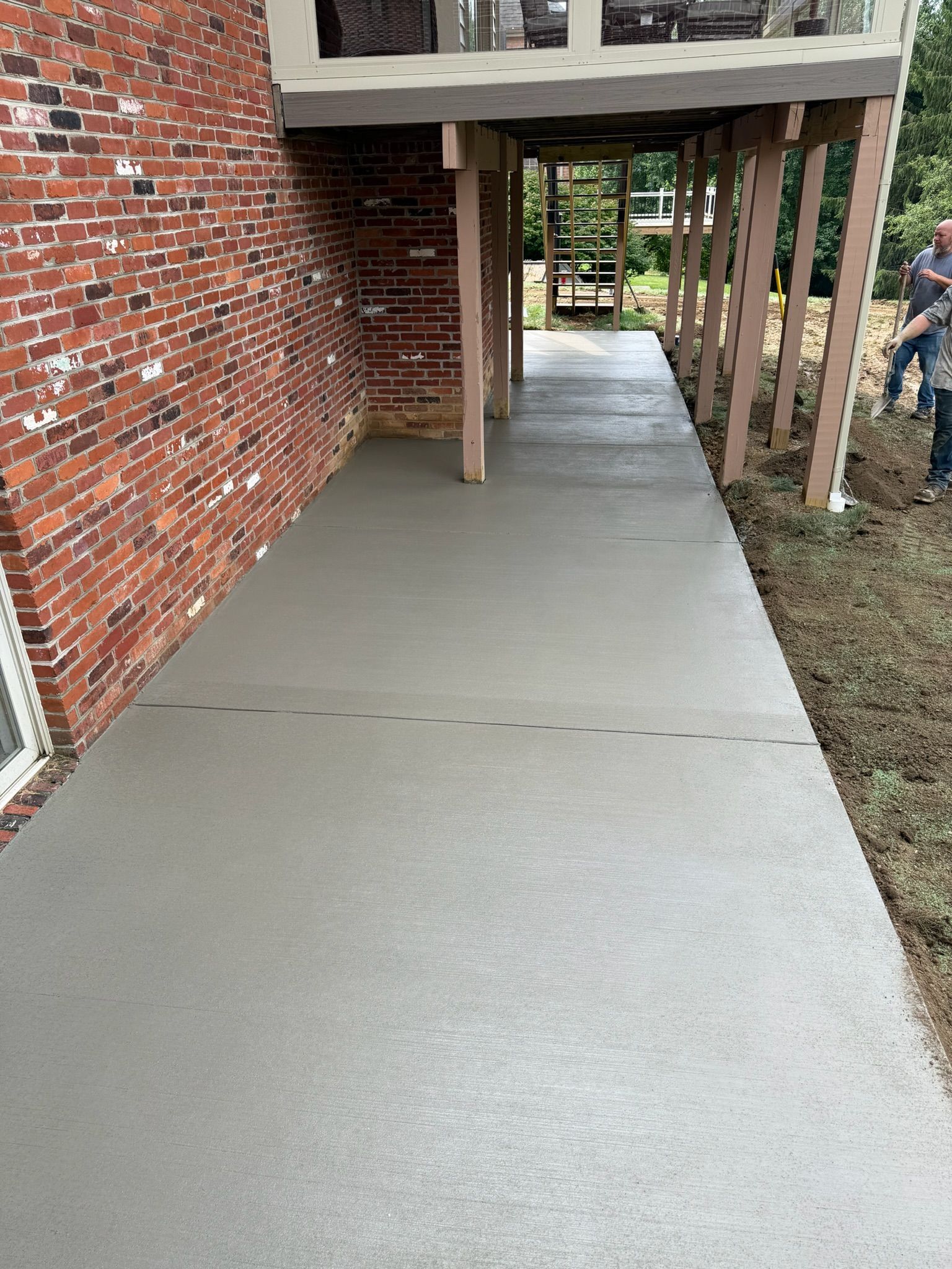 Covered concrete walkway beside a brick building with wooden posts and railings in a residential area