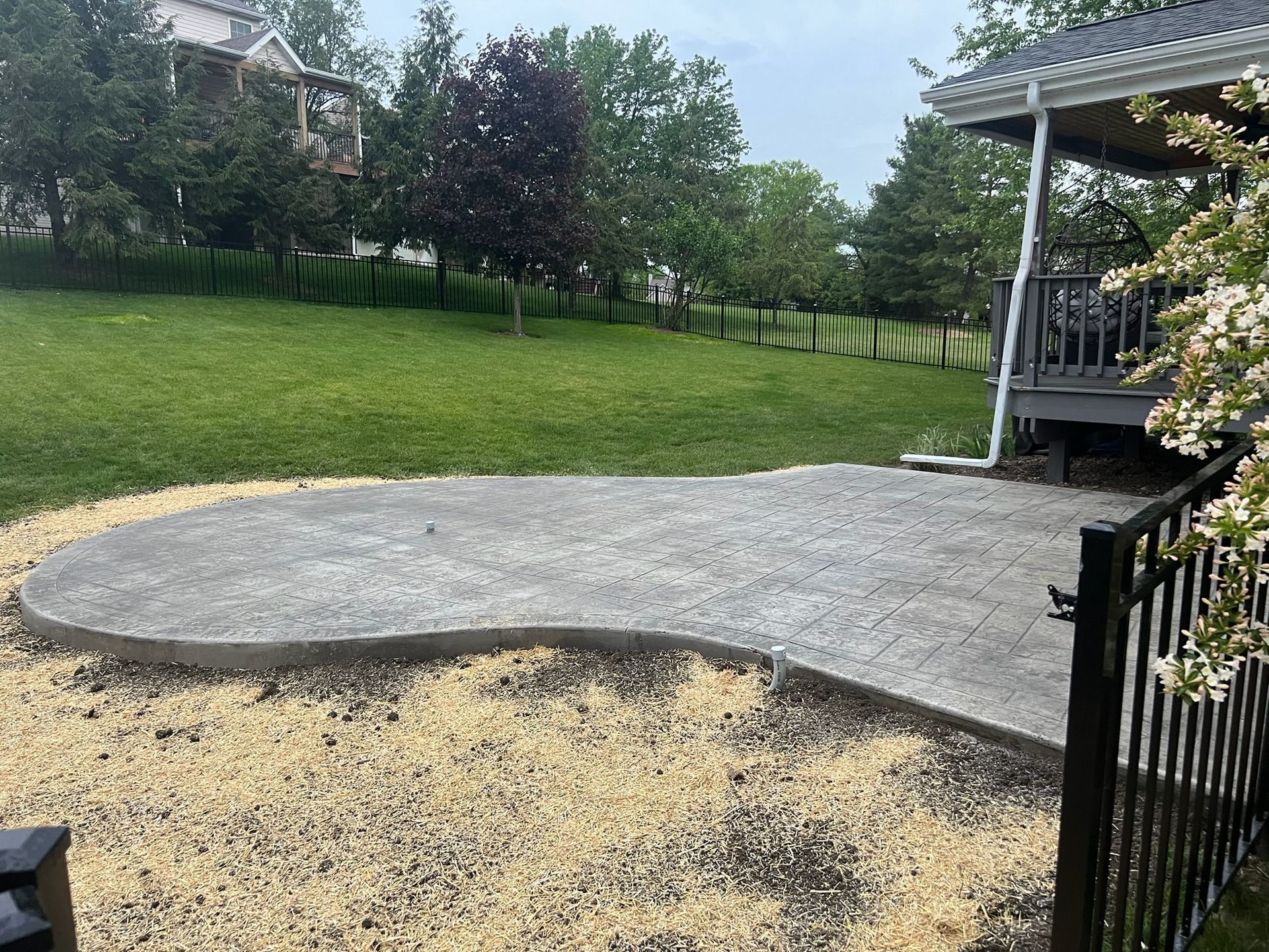 Backyard with a curved concrete patio beside a grassy yard and porch.