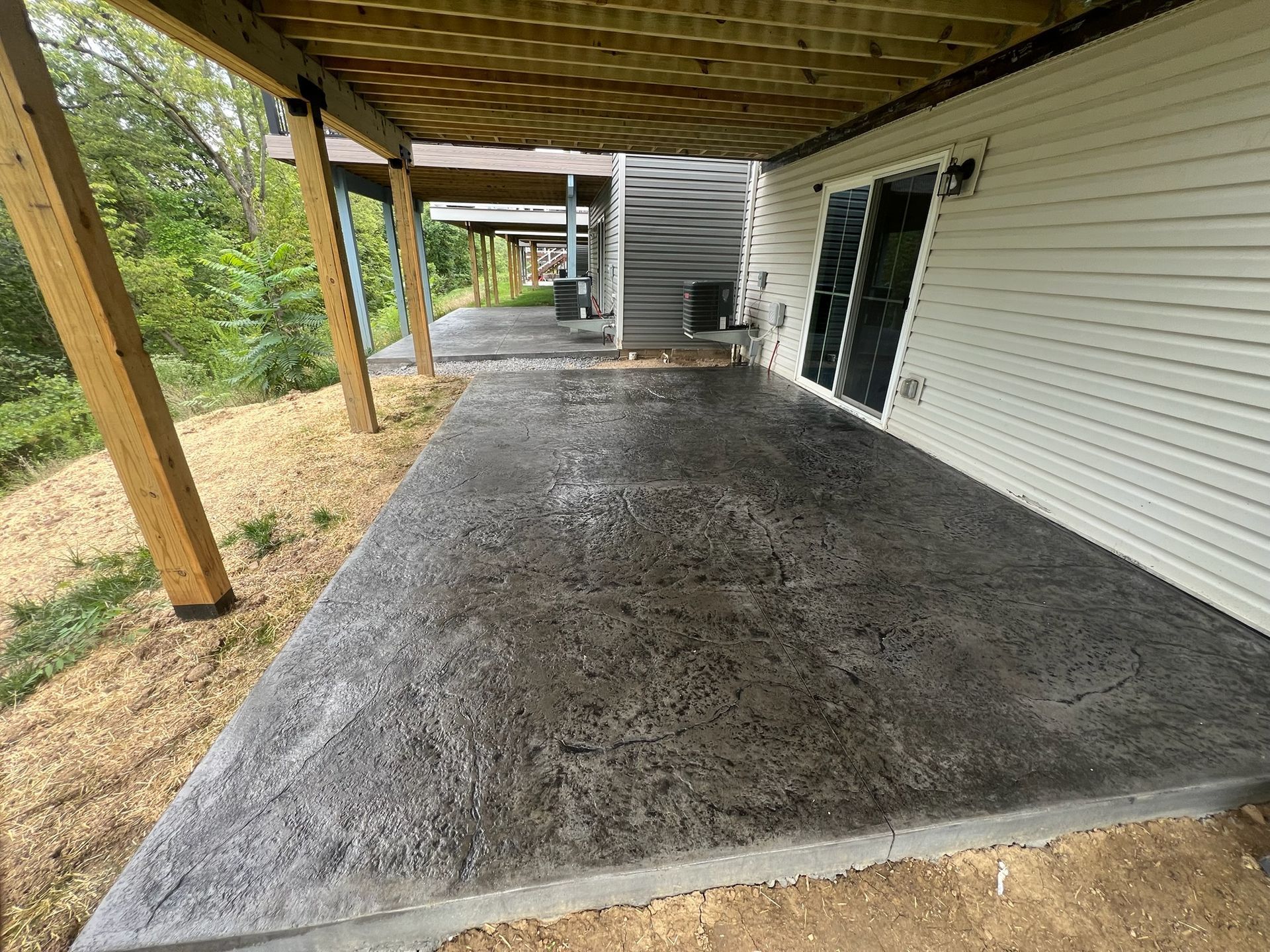 Covered concrete patio beside white-sided house, with wooden posts and a gravel edge.