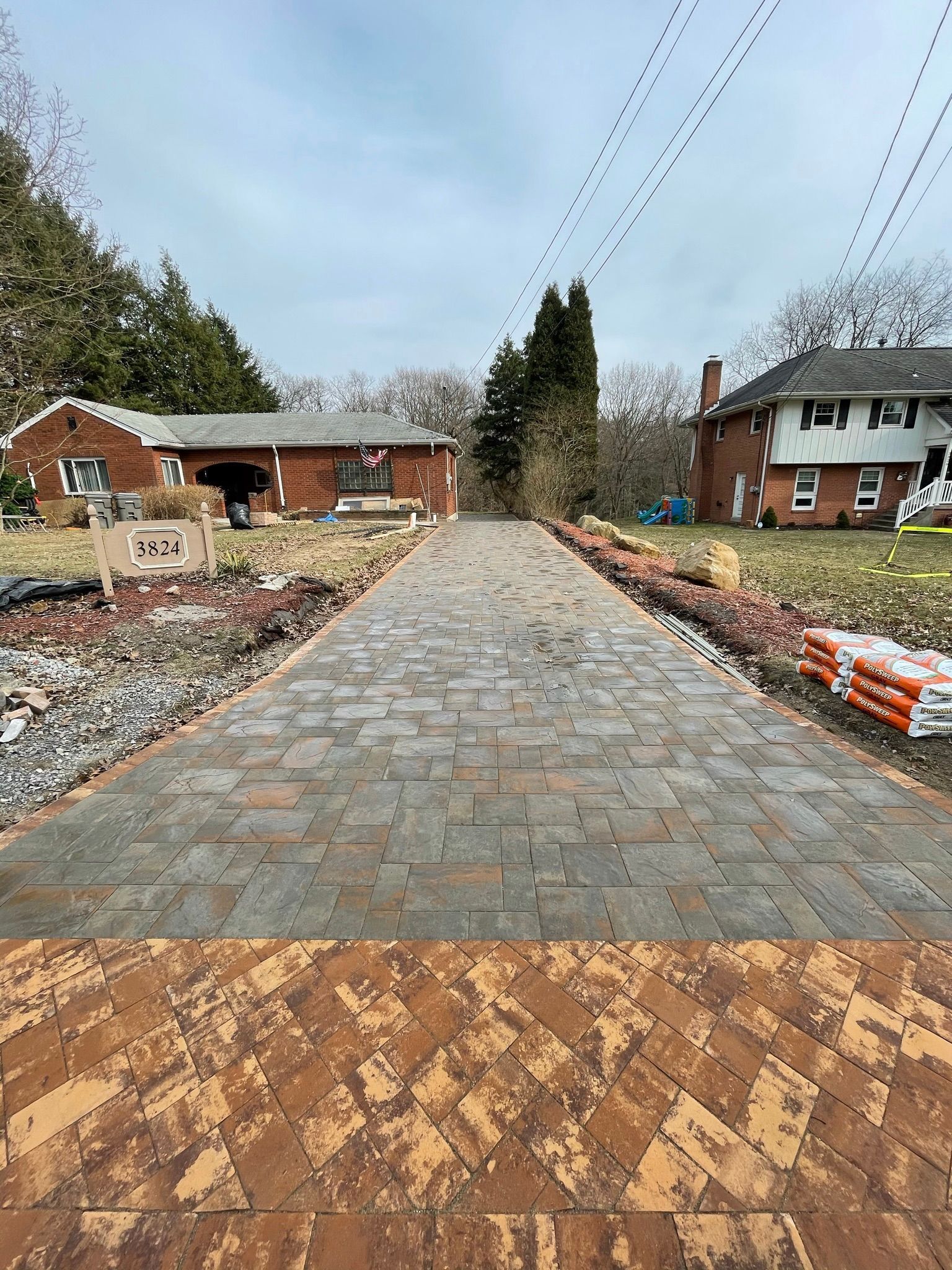 Stone driveway under construction leading to brick houses, with gravel borders and overhead utility lines.