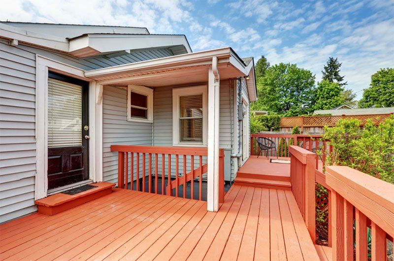 Red wooden deck with railing beside a house, featuring a small covered porch and sliding door