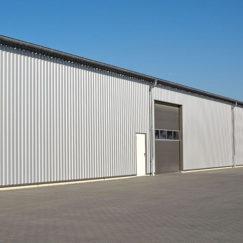 Large gray corrugated metal warehouse with a closed loading door under a clear blue sky