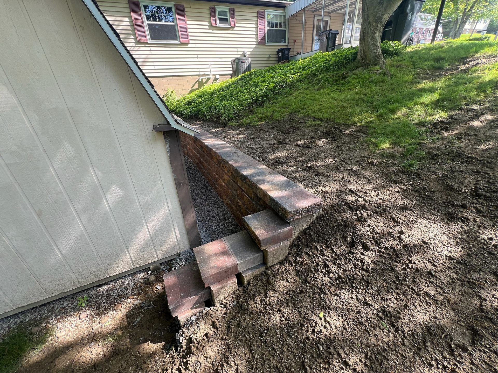 Small concrete steps beside a white shed on a sloped dirt yard, with a house in the background.
