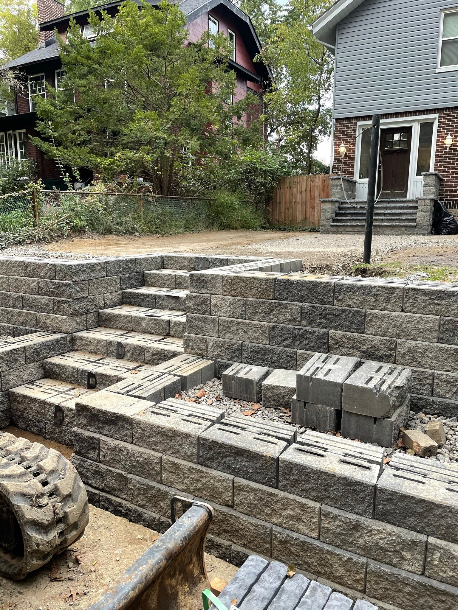 Tiered stone garden steps with low walls, small trees, and a house with a steep gray roof in the background