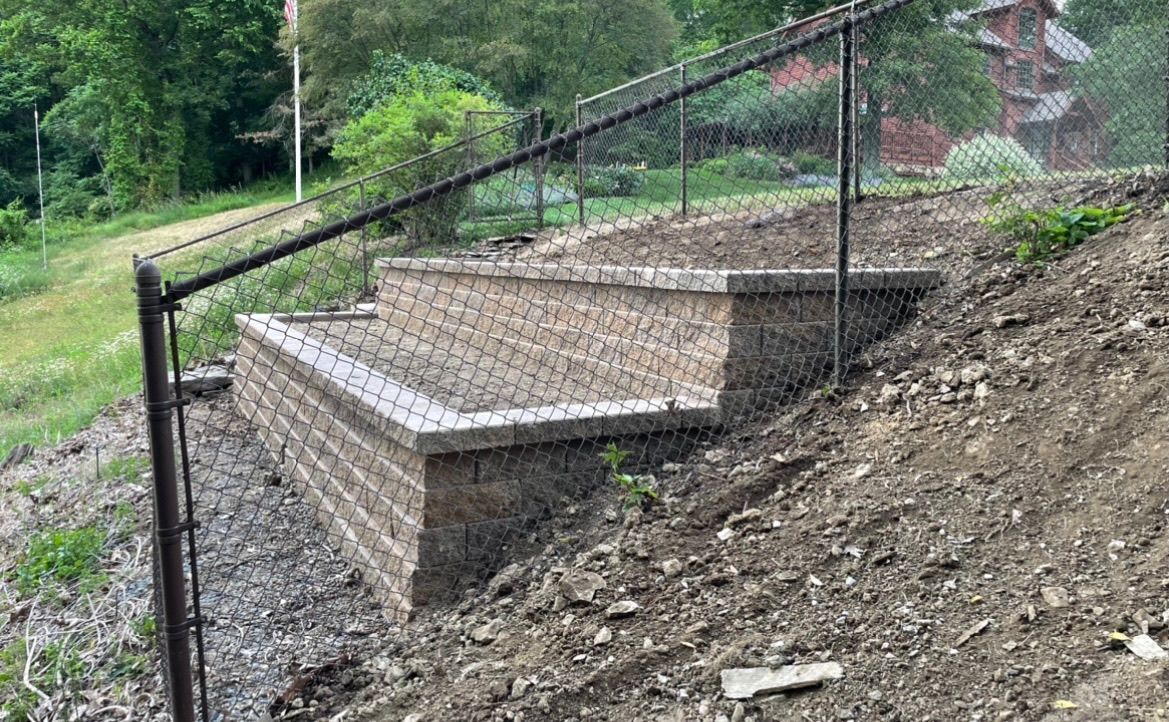 Concrete steps and retaining wall built into a sloped dirt hillside with a black rail fence.