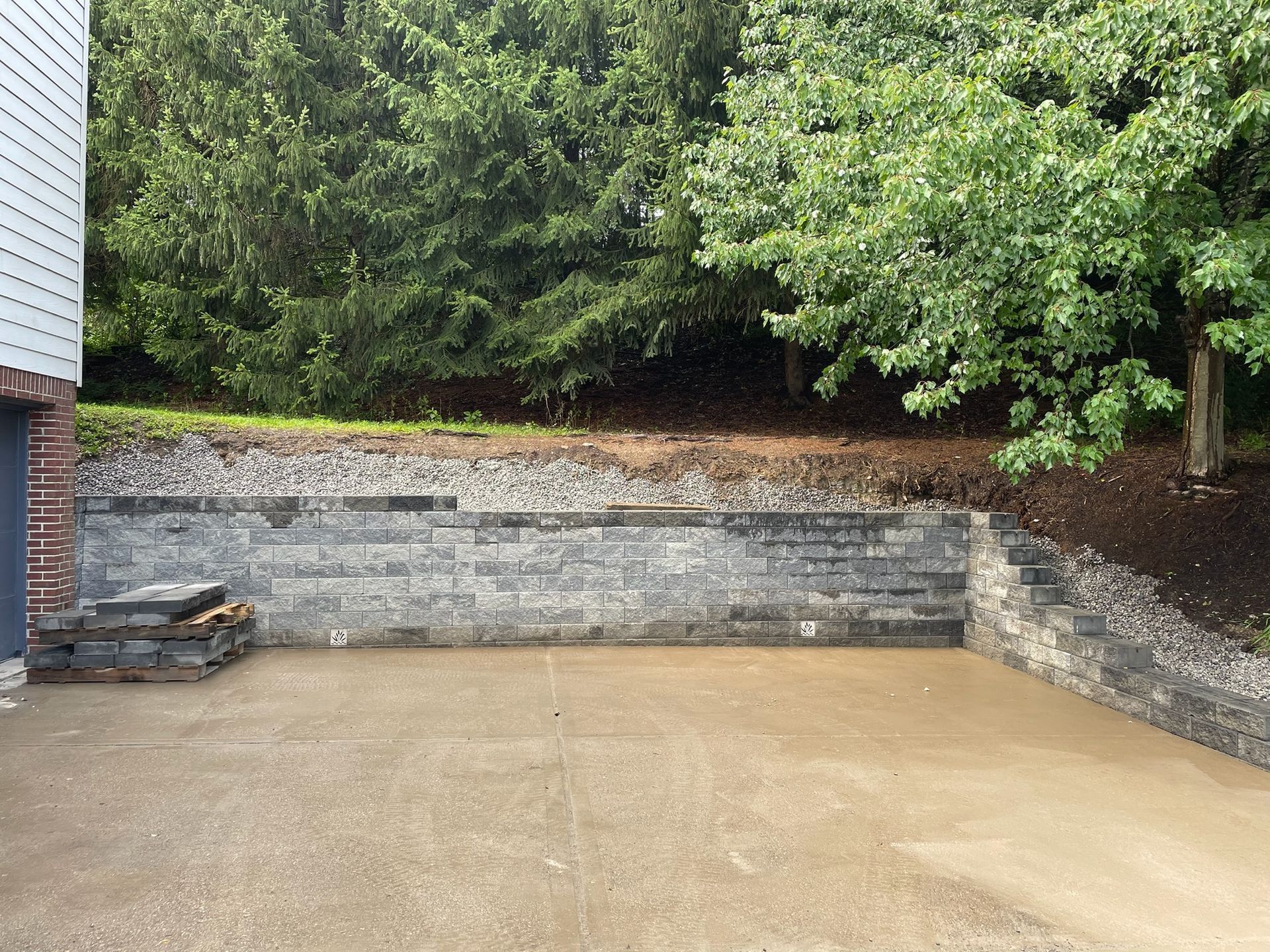 Empty concrete patio with stone retaining wall and trees behind it