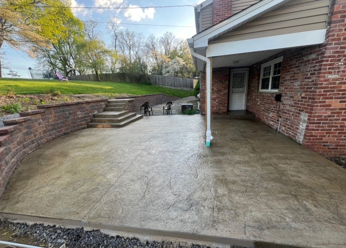 Covered brick patio with concrete floor, steps to a grassy yard, and a small dog in the distance