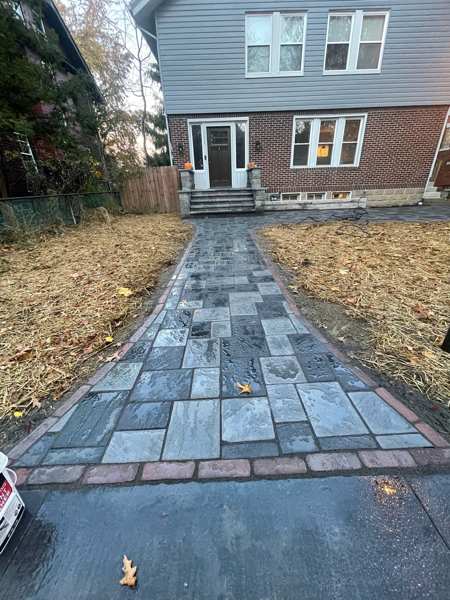 Stone walkway leading to a house entrance, bordered by fallen leaves in a front yard.