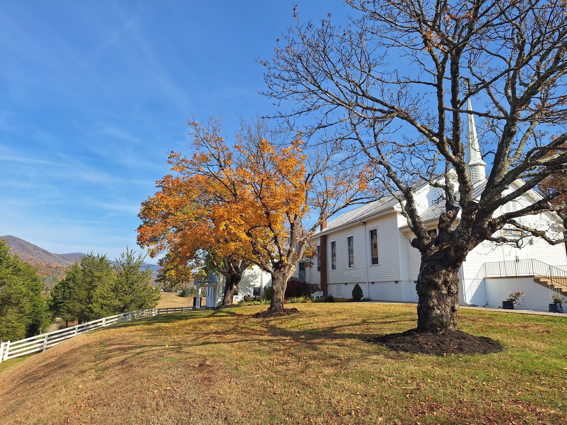 White church with spire, fall foliage, and blue sky.