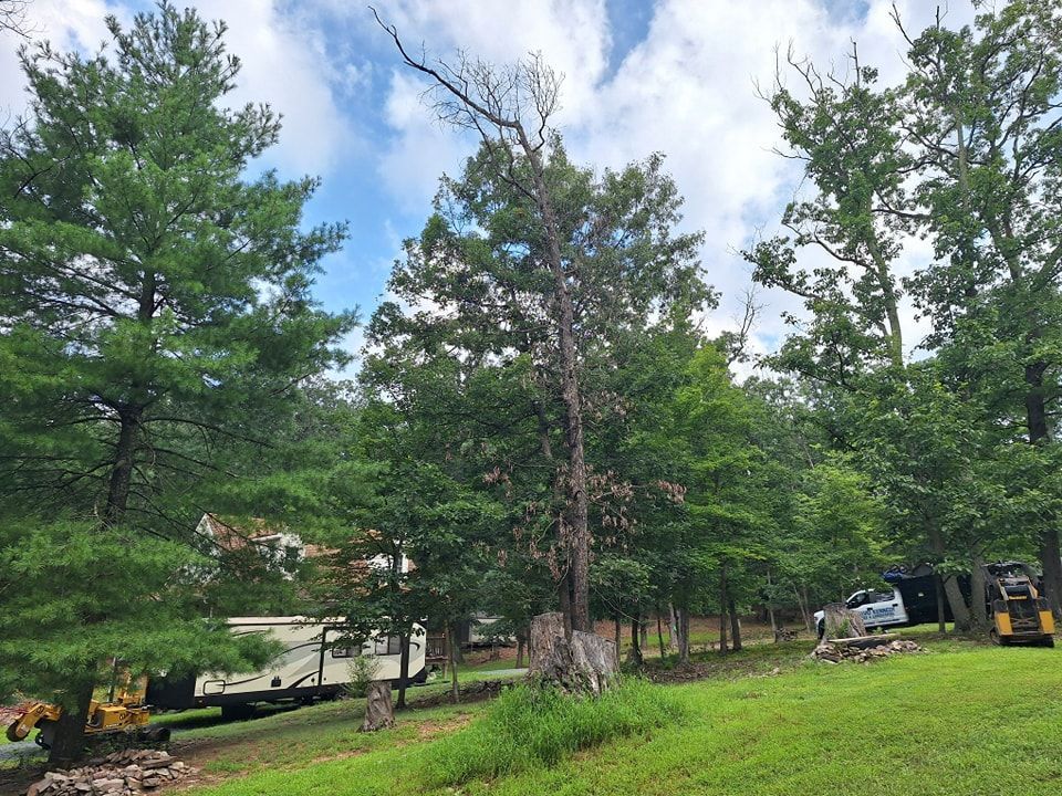 Lush green trees and grass under a partly cloudy sky. A camper and construction equipment are visible on the left.