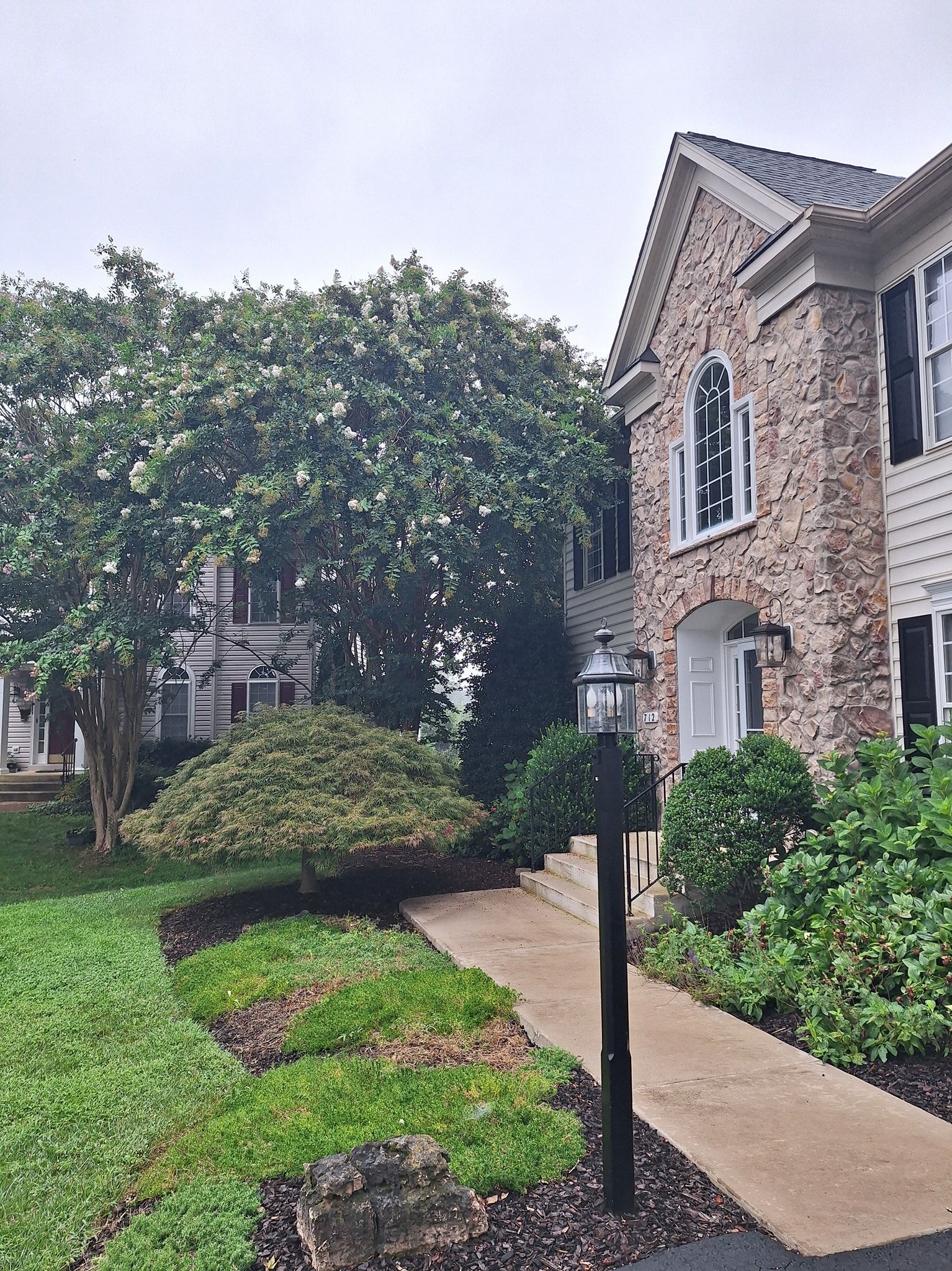 Brick and siding building with a walkway, lamppost, and landscaped yard on an overcast day.