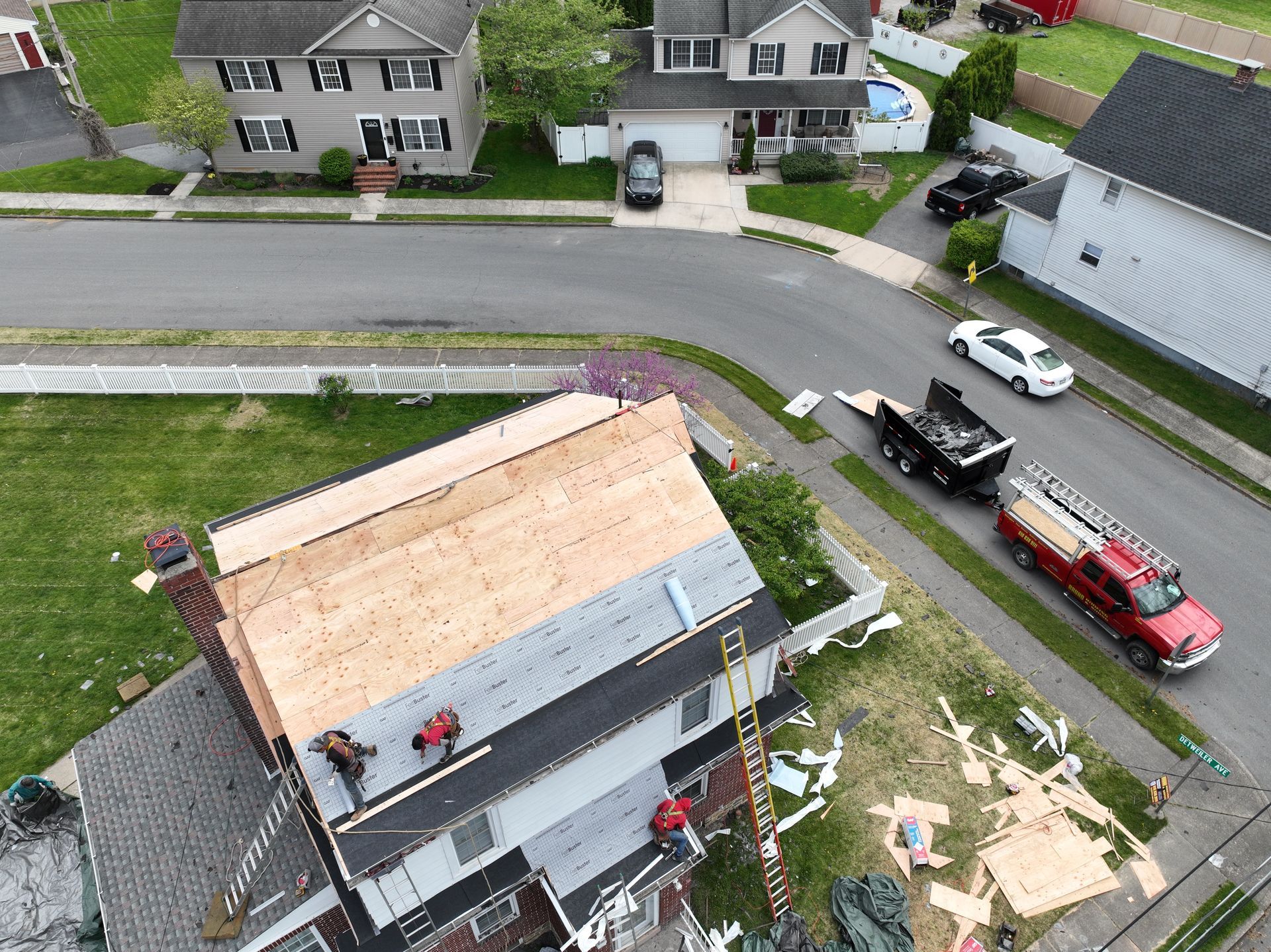 Aerial view of a house roof under repair with workers and a red truck parked nearby on a suburban street