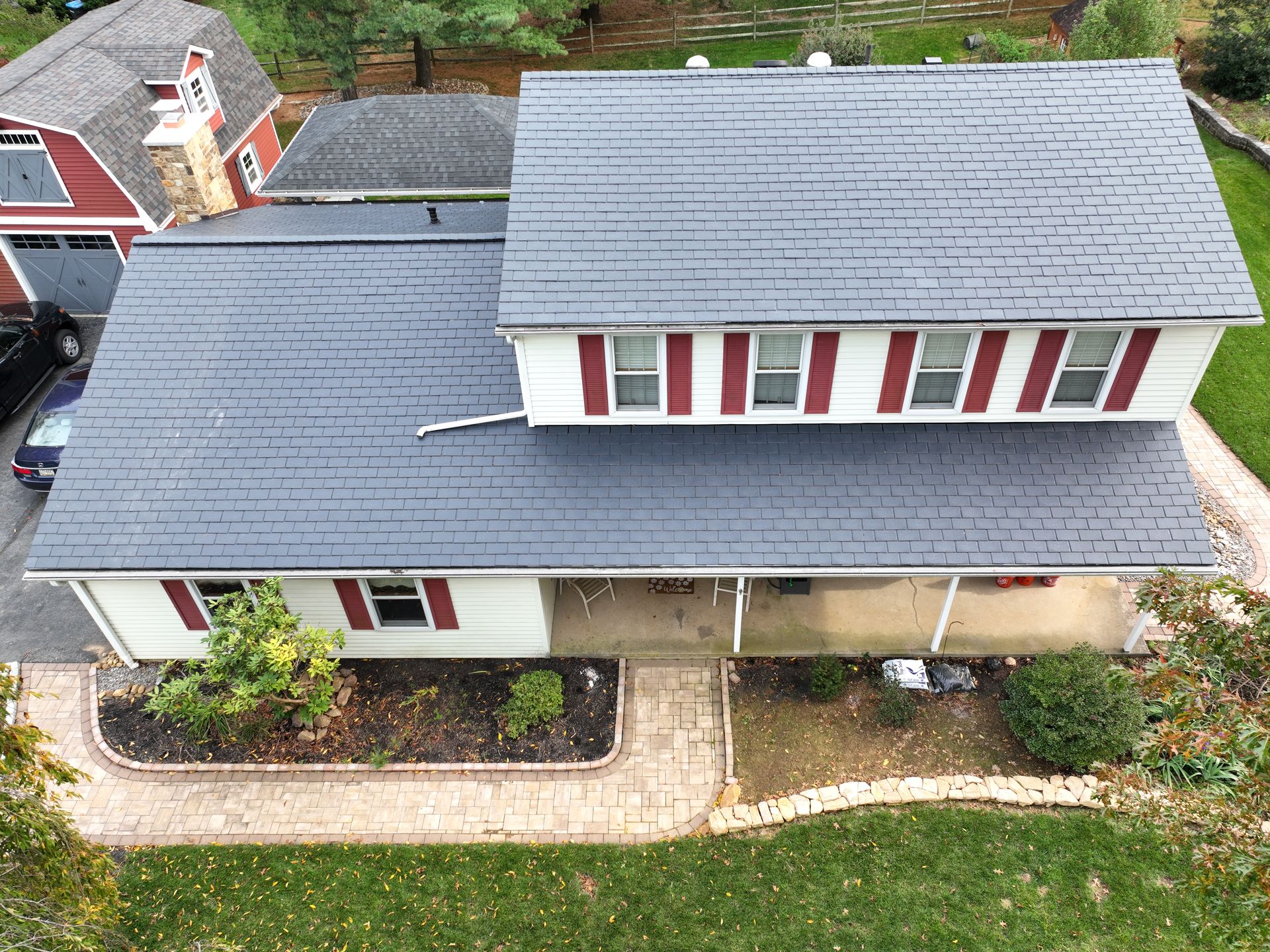 Aerial view of a two-story house with gray roof, red shutters, and a front walkway.
