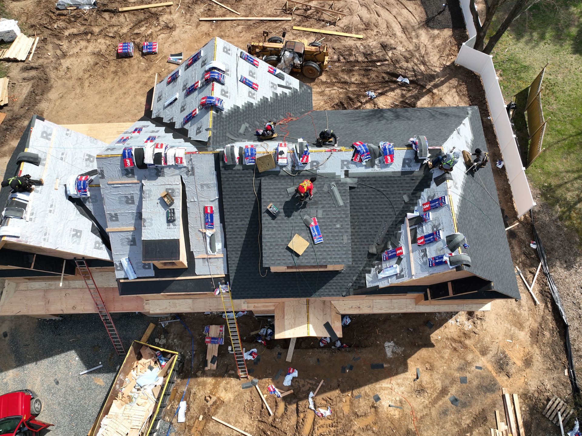 Aerial view of a house roof under construction with workers and materials scattered across the roof.