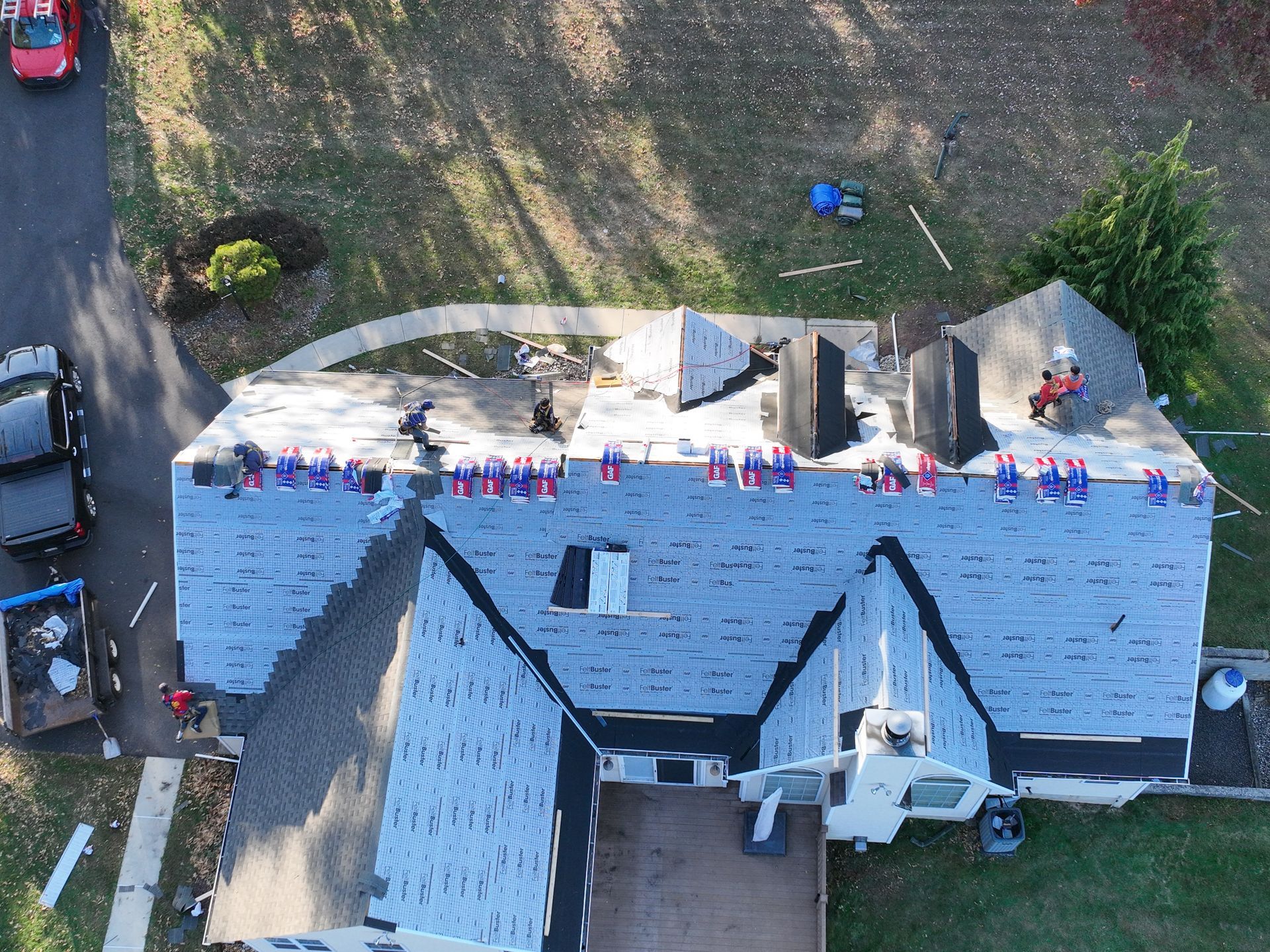 Aerial view of a house roof under repair with blue wrap, debris, and tools along the ridge line.