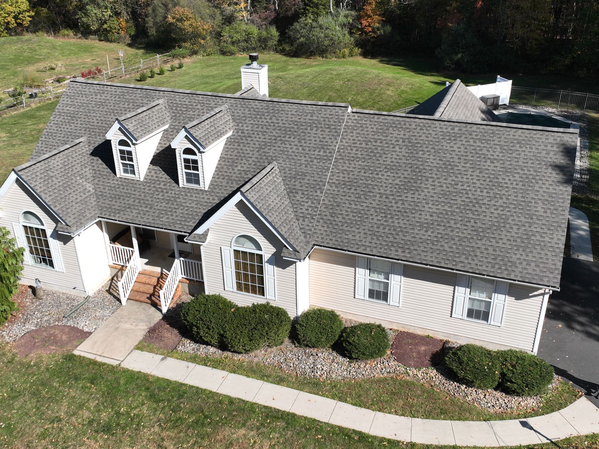 Aerial view of a gray suburban house with dormer windows, white trim, and a landscaped front yard.