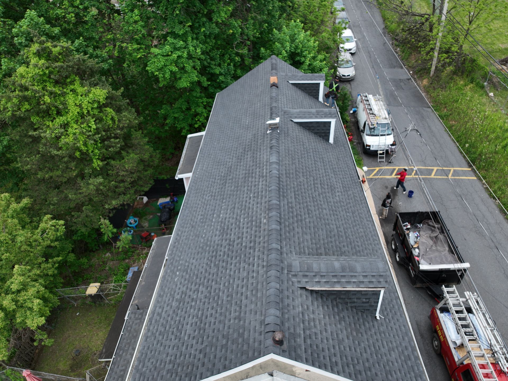 Aerial view of a house roof beside a road with utility trucks and workers nearby